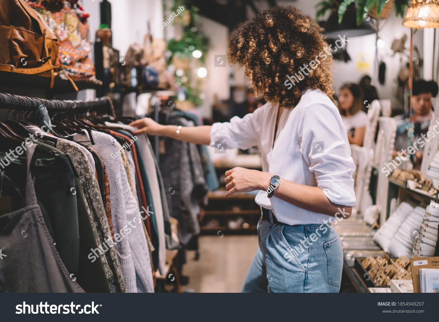Caucaisan female customer with curly hair buying clothes in boutique using fitting concept while choosing, professional stylist creating trendy look concentrated on selection in designer shop #1854949207