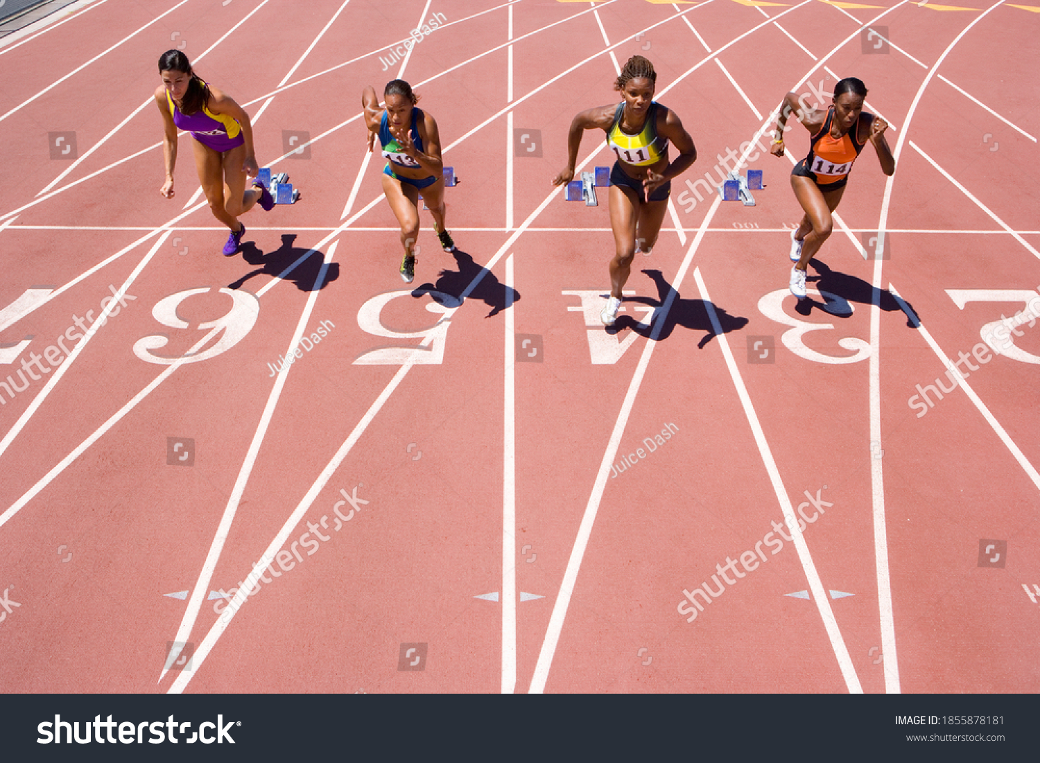 Female athletes setting off from their starting blocks at the start of a sprint race at an athletics competition at the track #1855878181