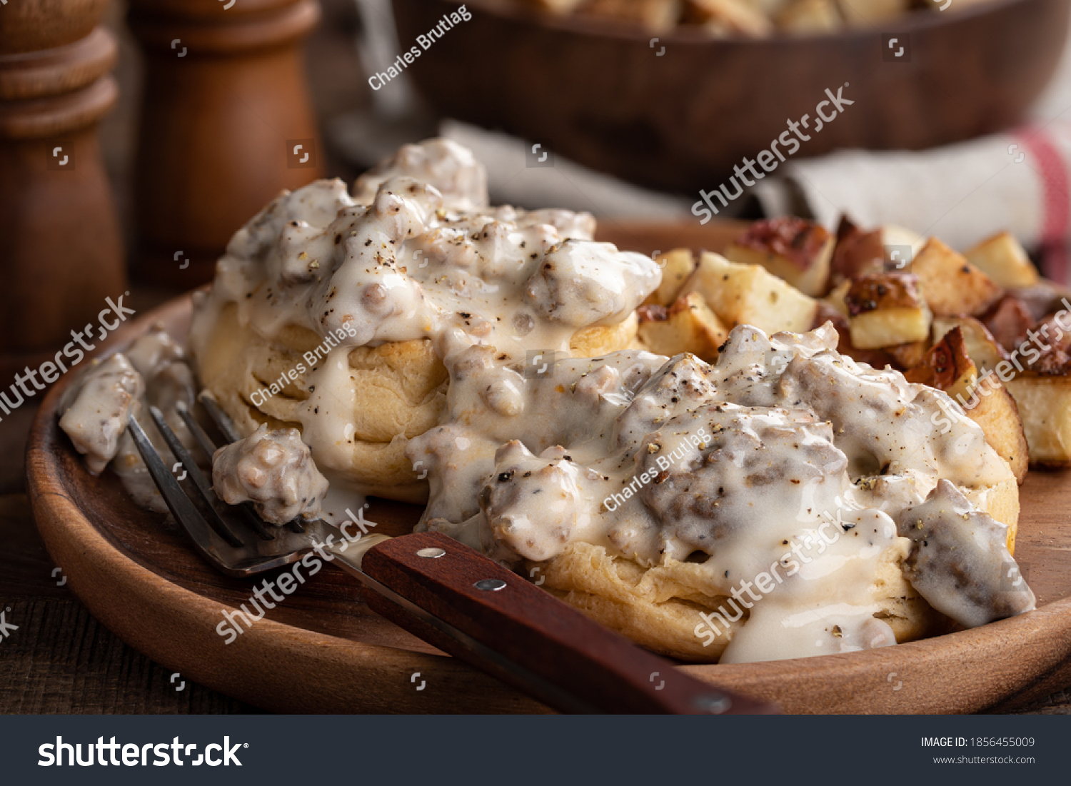 Closeup of biscuits with creamy sausage gravy and fried potatoes on a wooden plate #1856455009