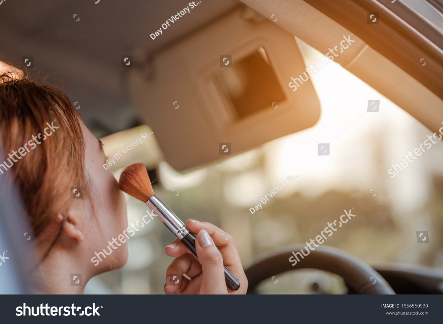 Asian women applying makeup in interior car  with looking mirror using brush make up.
She hurriedly put on makeup on the car to catch up to work.Holiday,travel and vacation concept. #1856560939