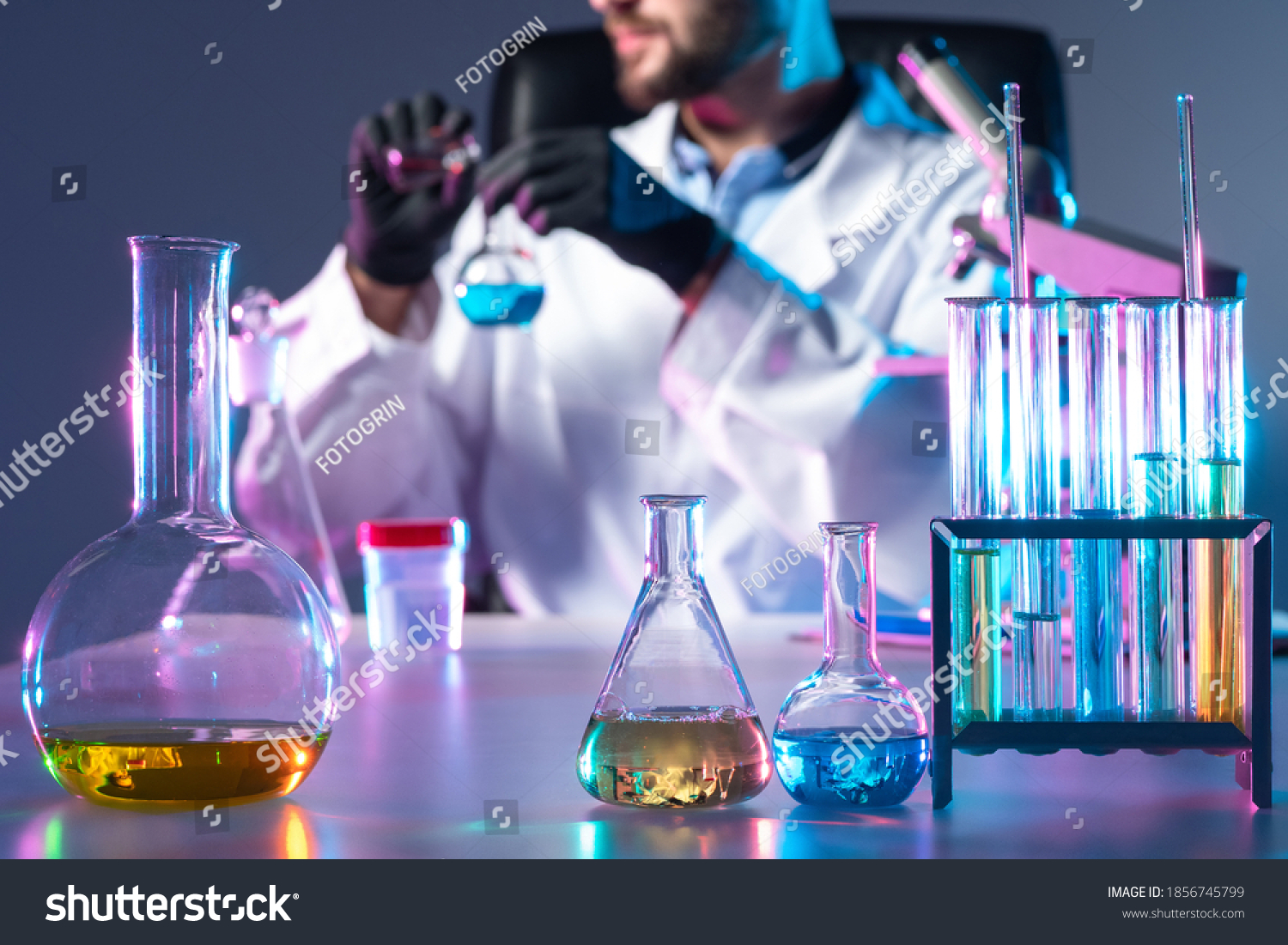 Doctor creates vaccine. Test tubes next to laboratory assistant. Doctor in background mixes liquid in test tubes. Medicine for virus is in lab glussware. He synthesizes vaccine. Vaccine test concept #1856745799