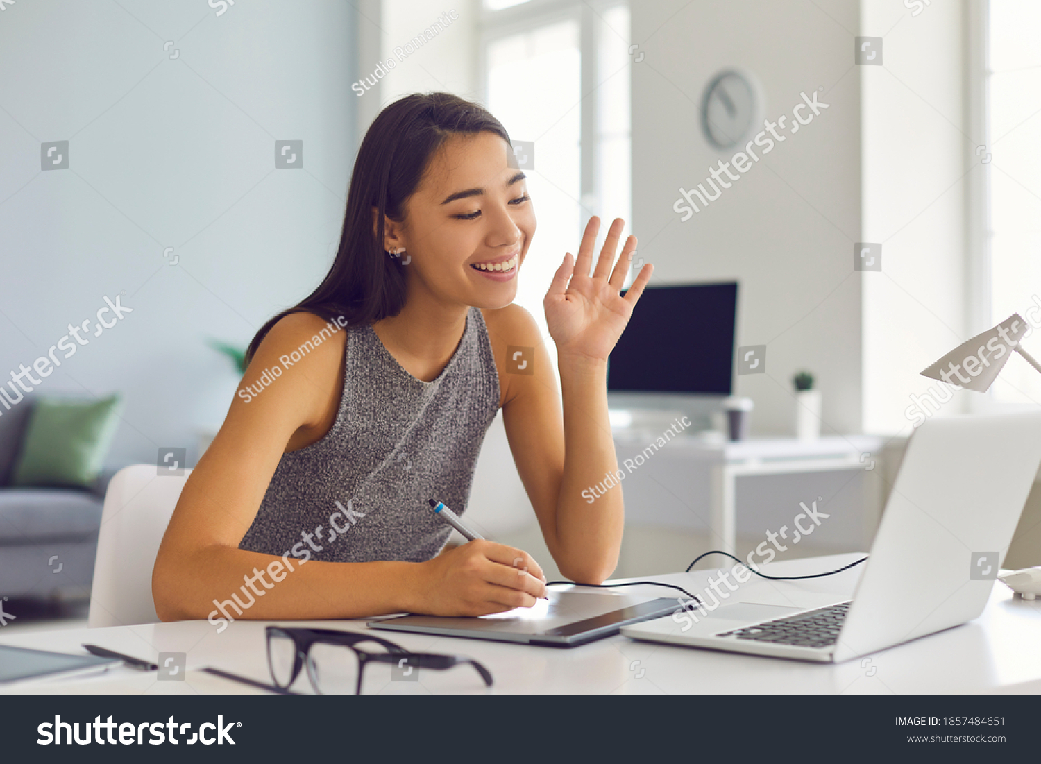 Smiling creative young digital artist girl with graphic tablet and pen waving hand at laptop computer, meeting client online from home office and painting or drawing sketch portrait via video call app #1857484651