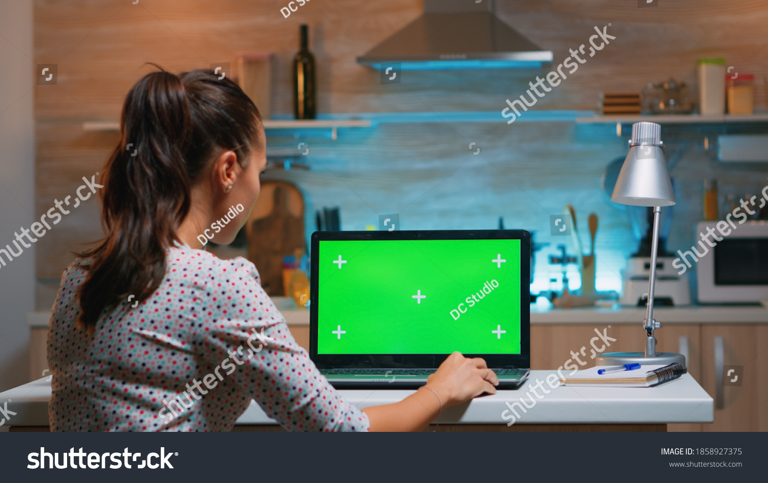 Business woman looking at green screen laptop sitting at home in kitchen. Freelancer watching desktop monitor display with green mockup, chroma key, during night time working overtime. #1858927375