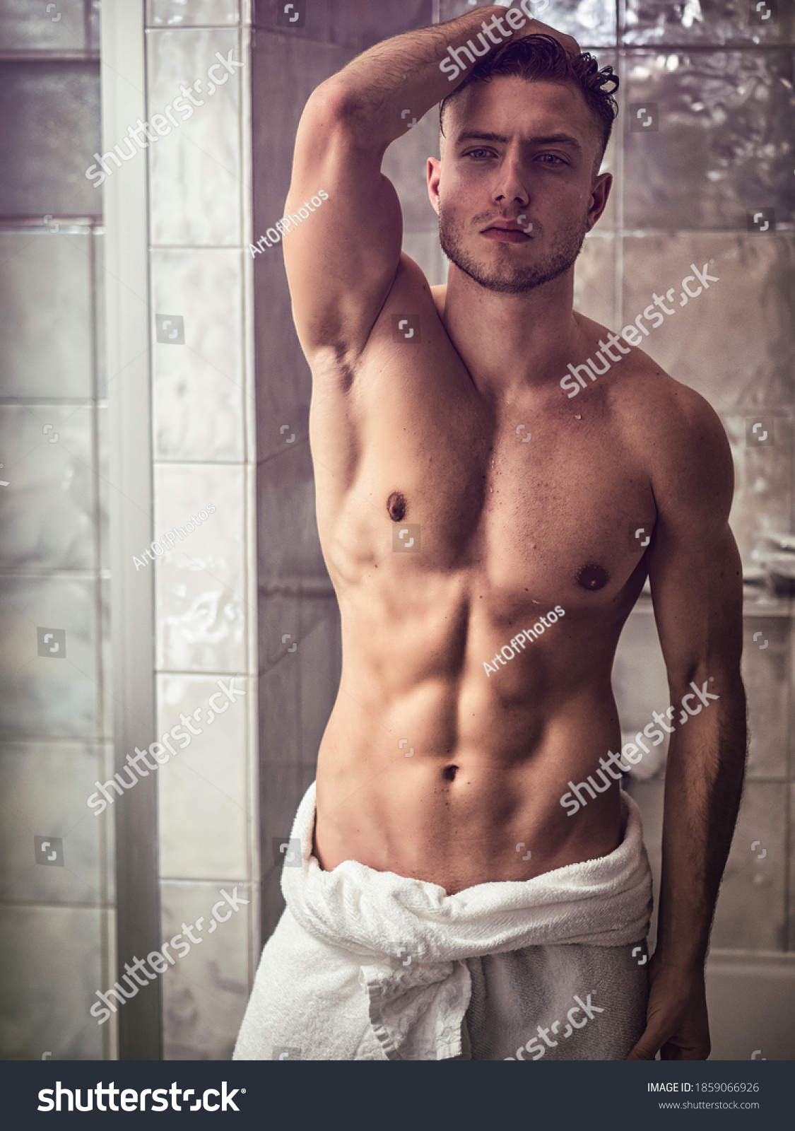 Shirtless muscular handsome man looking at himself in bathroom mirror in the morning after shower or bath, with towel around his waist #1859066926