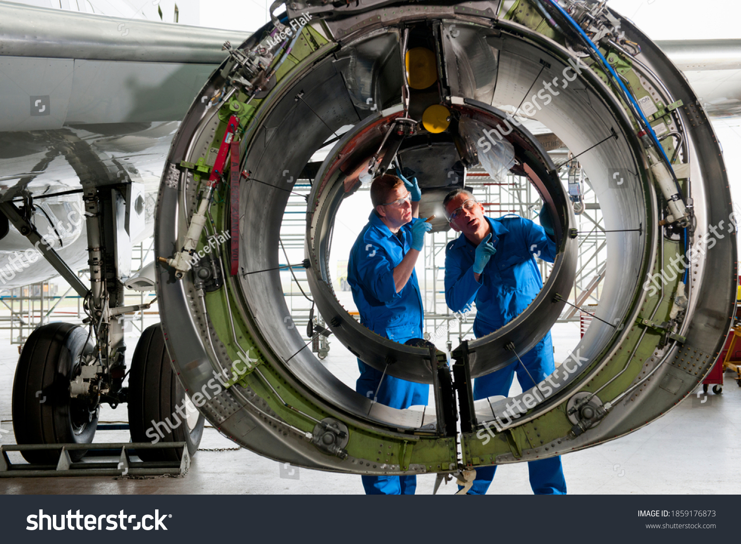 Engineers in uniforms inspecting the engine casing of a passenger jet at a hangar. #1859176873
