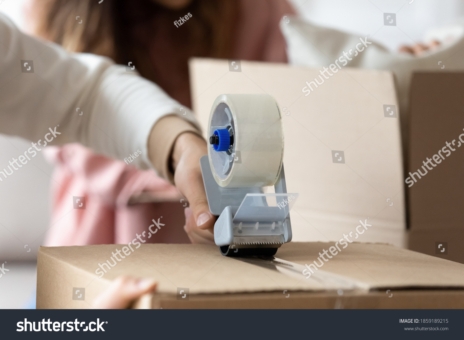 Man holding tape dispenser sealing cardboard box with personal stuff belongings on happy moving day to own house. Family prepare parcel, send cheap services ad, relocation to new apartment concept #1859189215