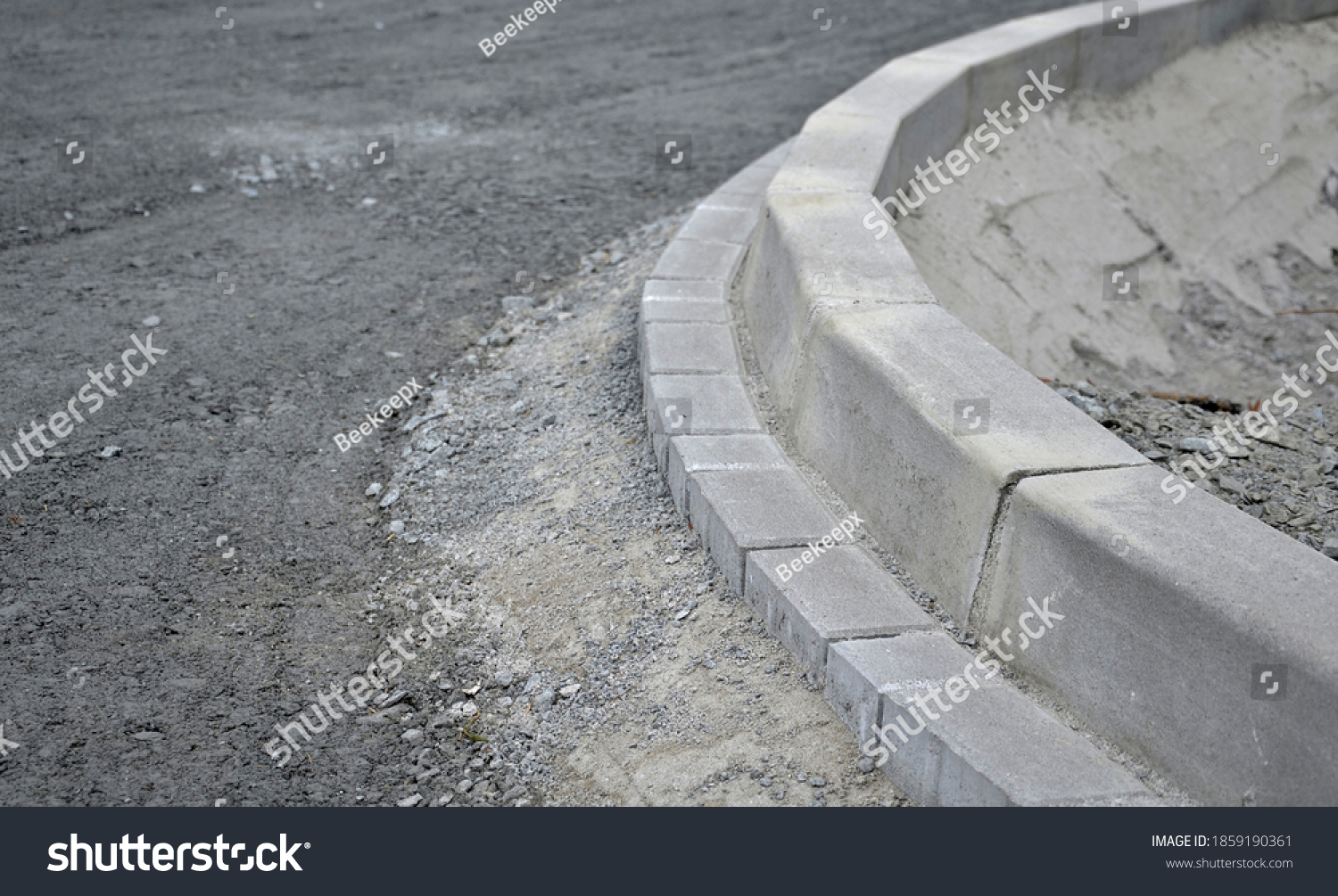 installation of concrete curb into concrete. in the space of the road, which so far has only a concrete base before laying the asphalt layer and rolling. #1859190361