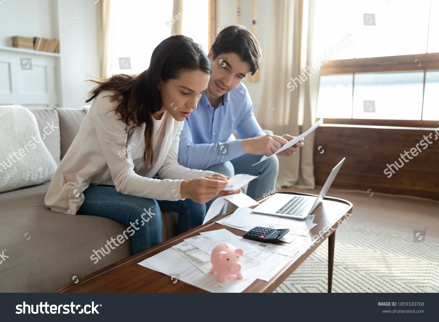 Taking close look at paper. Concentrated attentive millennial couple sitting at home office in living room involved in reading documents preparing to provide loan mortgage utility bills payment online #1859320768