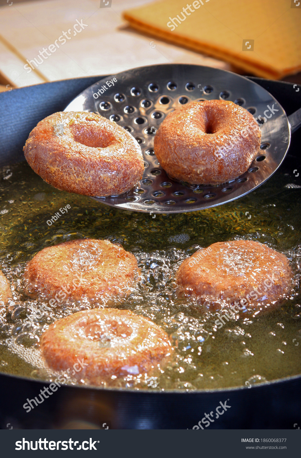 Freshly made donuts coming out of the frier pan and some still cooking in the hot oil. #1860068377