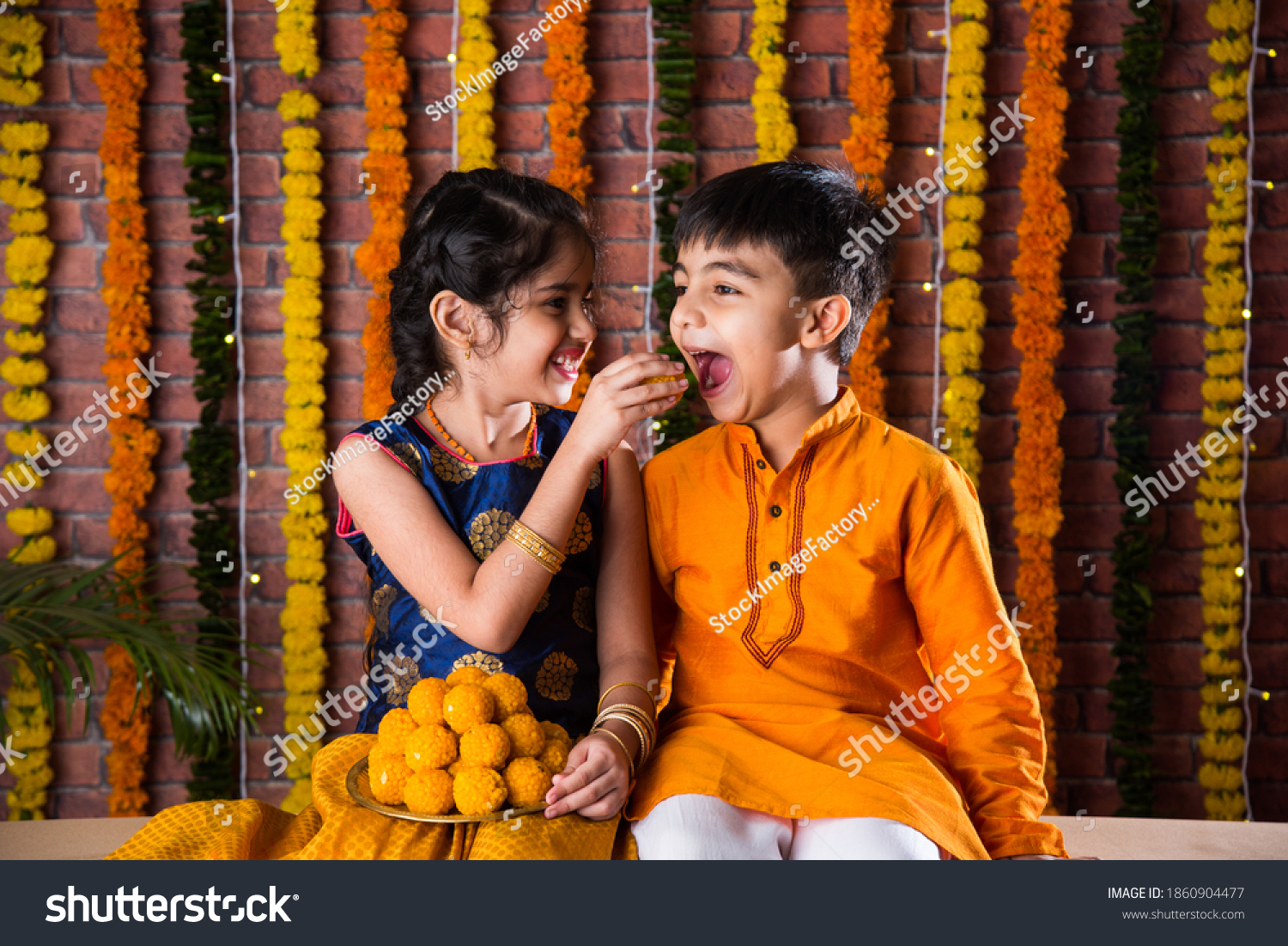 Indian kids, little brother and sister celebrating Diwali, Raksha Bandhan, Bhai Dooj with big gift box and sweet laddoo #1860904477