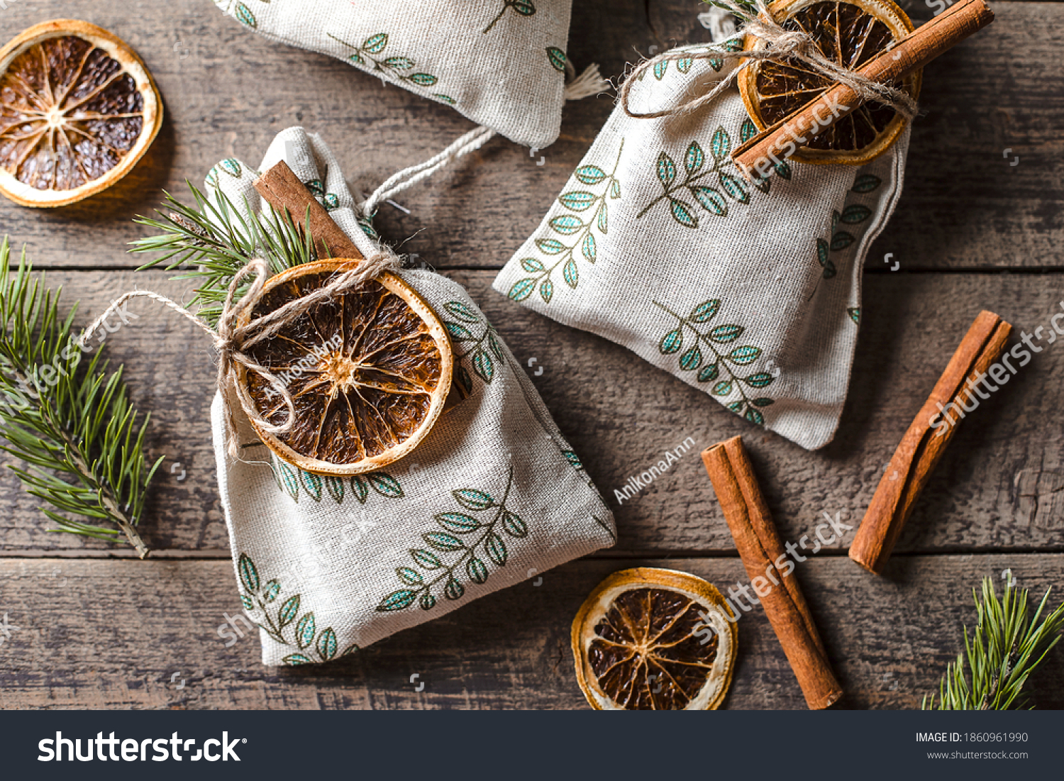 Christmas still life with eco friendly textile gift packaging. Fabric gift pouches decorated by fir tree, dry citrus and cinnamon stick's. #1860961990