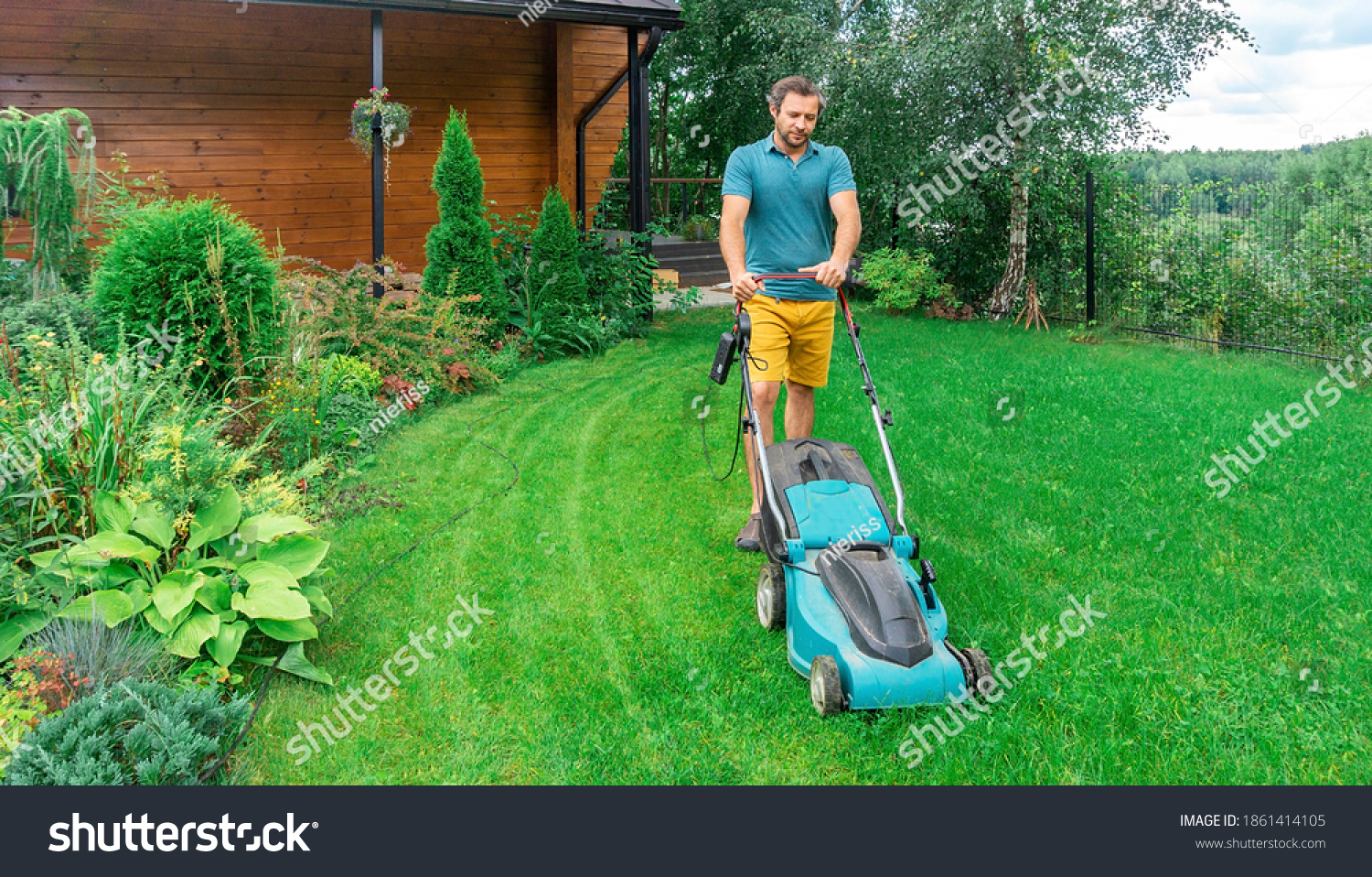 Lawn care. Mowing grass with an electric lawn mower. A young man mows the grass with a lawn mower with a grass collector on a sunny summer day. Beautiful landscape design in the garden. #1861414105