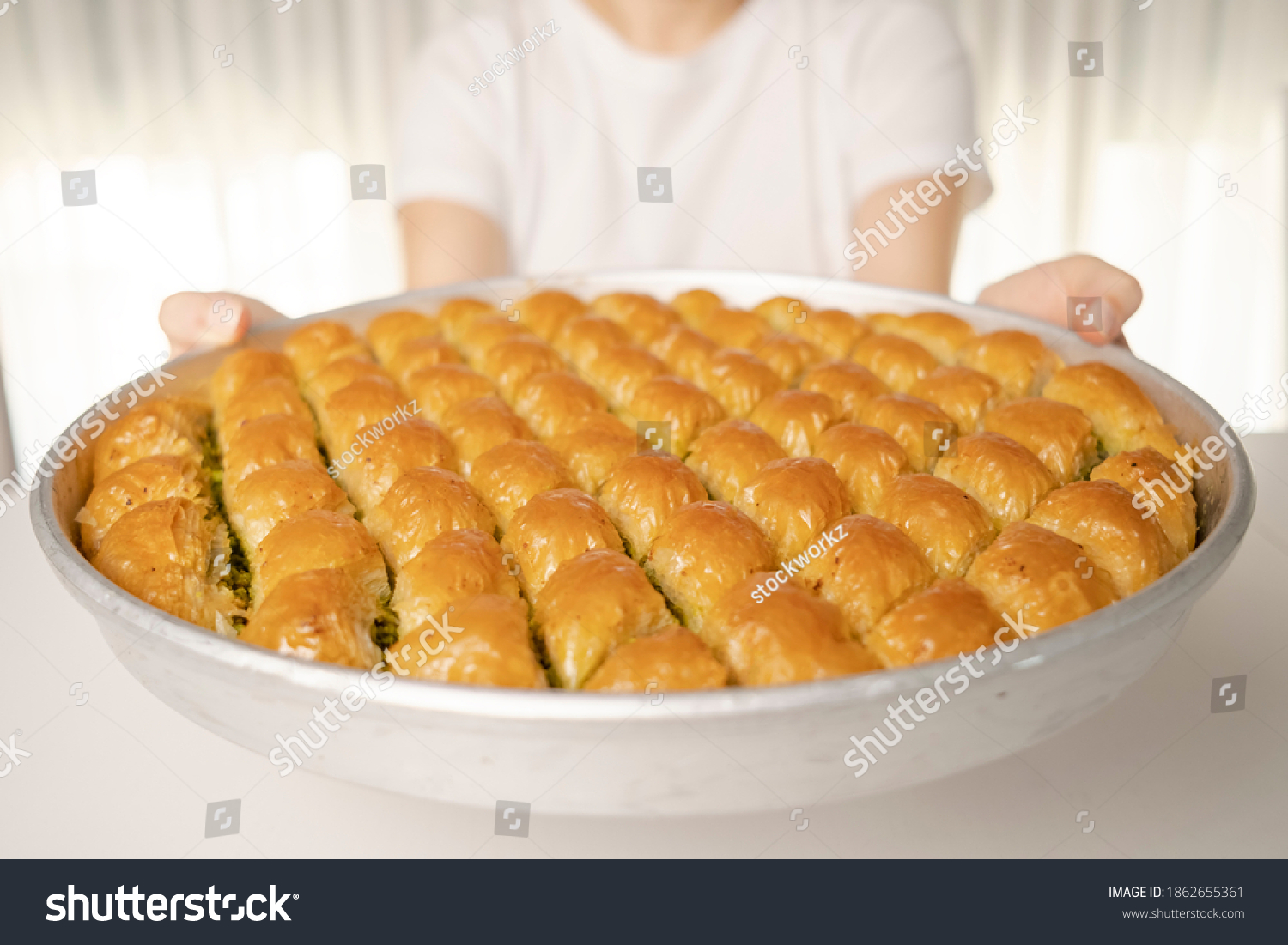 Close detail shot of a tray of crispy baklava dessert in the background white t-shirt woman holding the tray in her hand #1862655361
