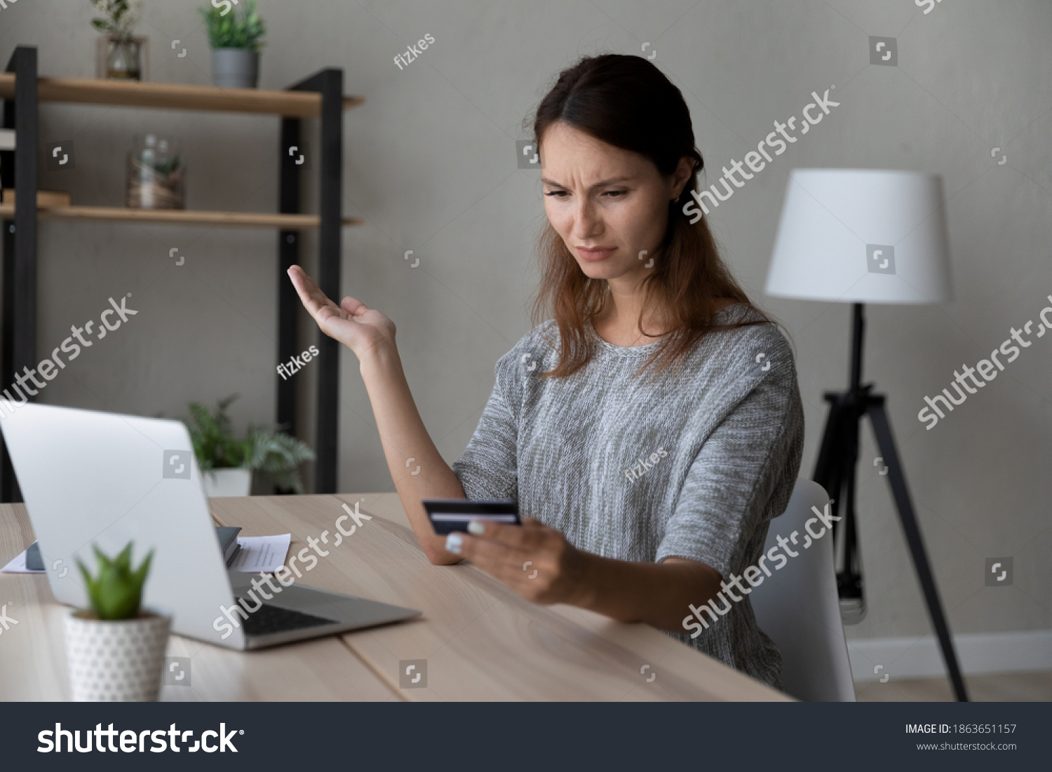 Confused young woman holding credit card in hands, stressed by financial payment mistake, blocked e-banking account or low quality money transfer service, feeling insecure shopping online at home. #1863651157