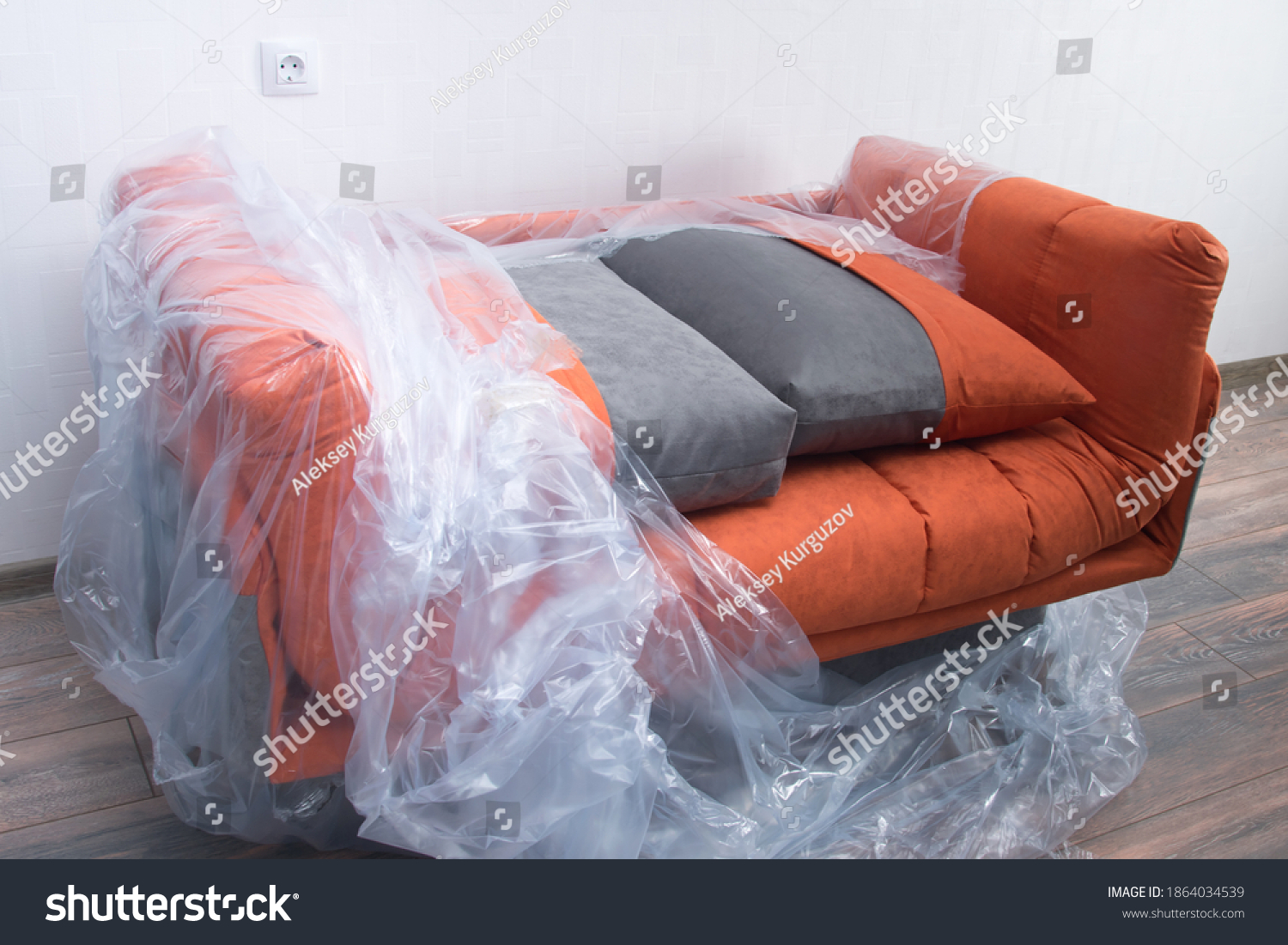 there is an orange sofa in the room, partially covered with plastic wrap to protect it from dirt and dust #1864034539