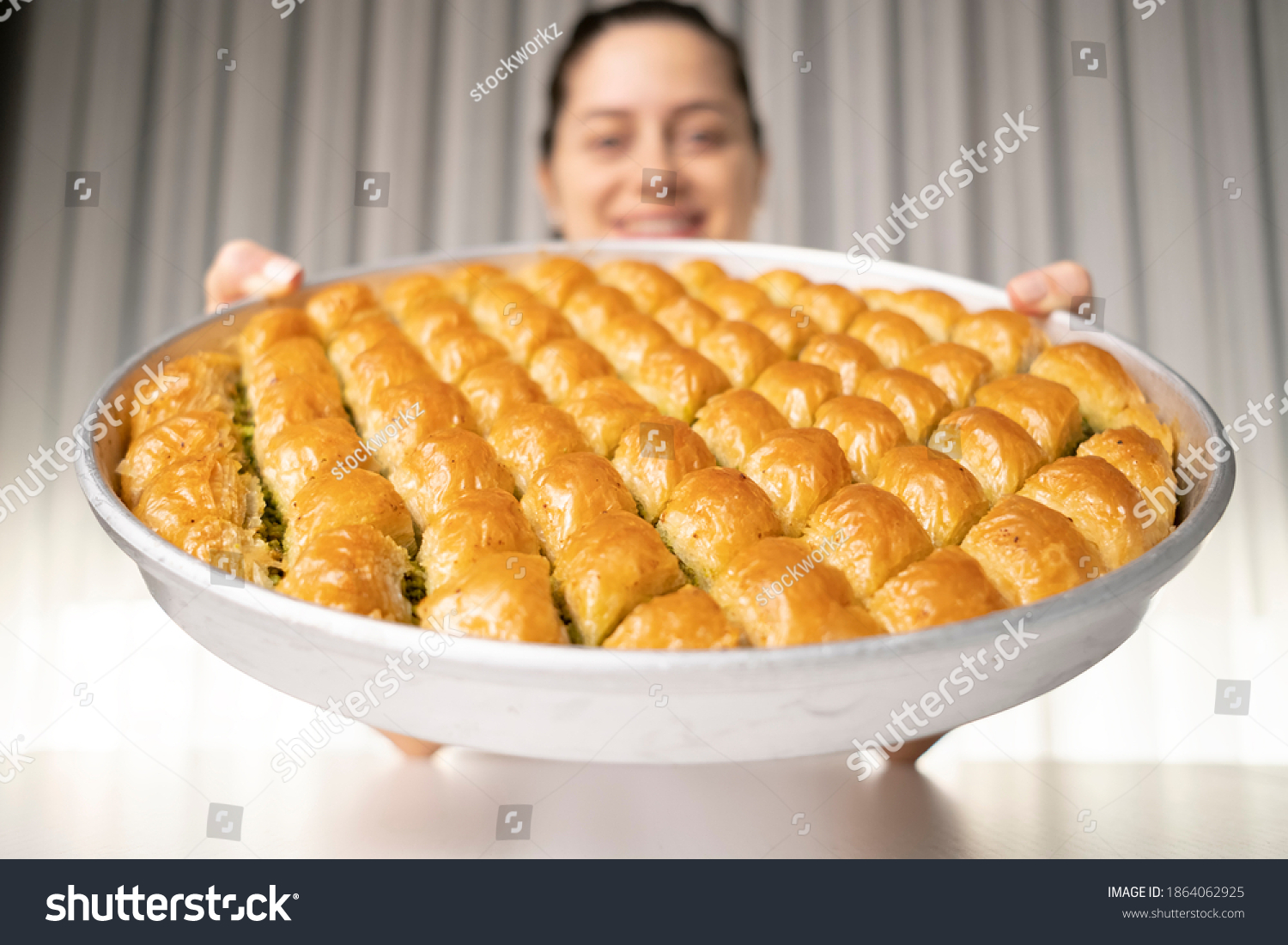 She lifts the tray of baklava dessert in her hand and smiles at the camera deep in the field #1864062925