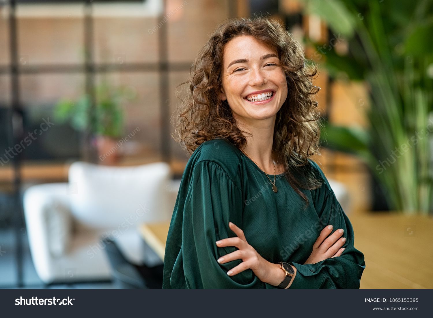 Portrait of young smiling woman looking at camera with crossed arms. Happy girl standing in creative office. Successful businesswoman standing in office with copy space. #1865153395