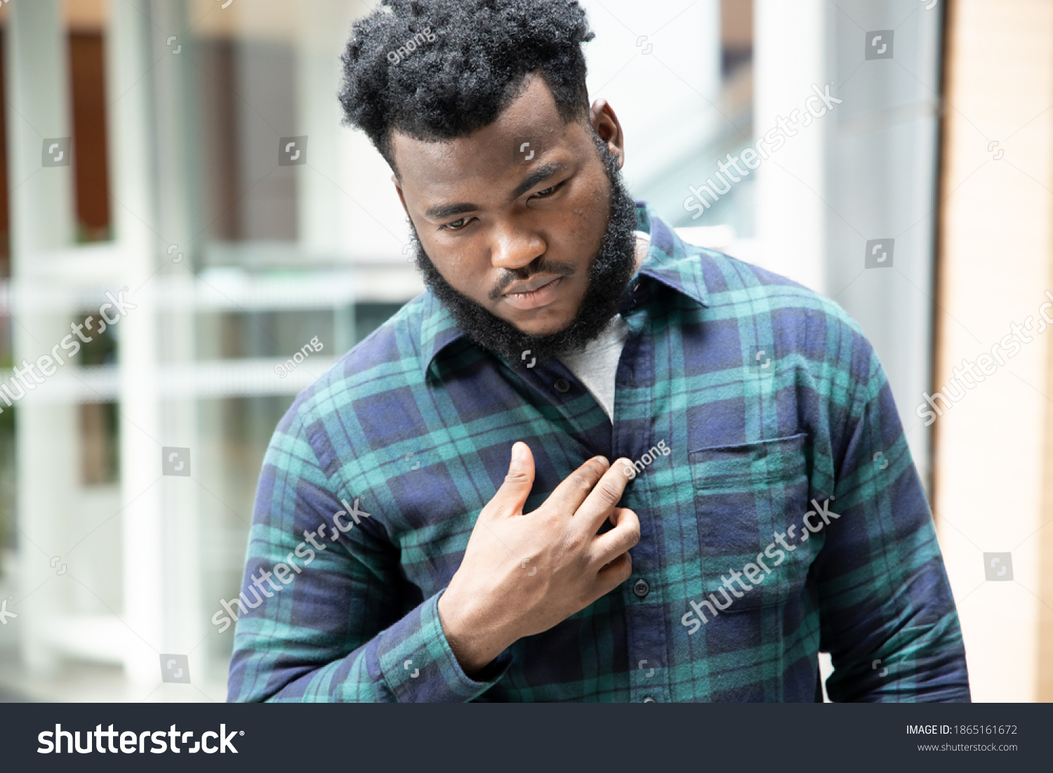 African man suffering from acid reflux or GERD; sick stressed black man with indigestion, acid reflux or gerd symptoms; man health care, body care, sickness, pain concept; adult african man model #1865161672