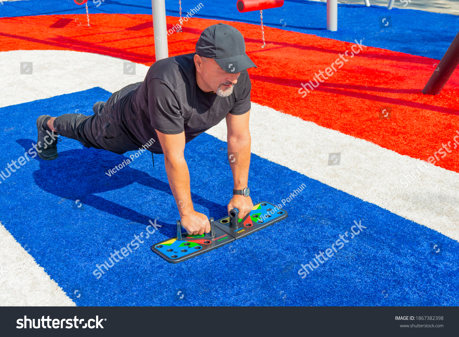 Athletic man doing push-ups on a push-up board at the sports field in the city park. #1867382398