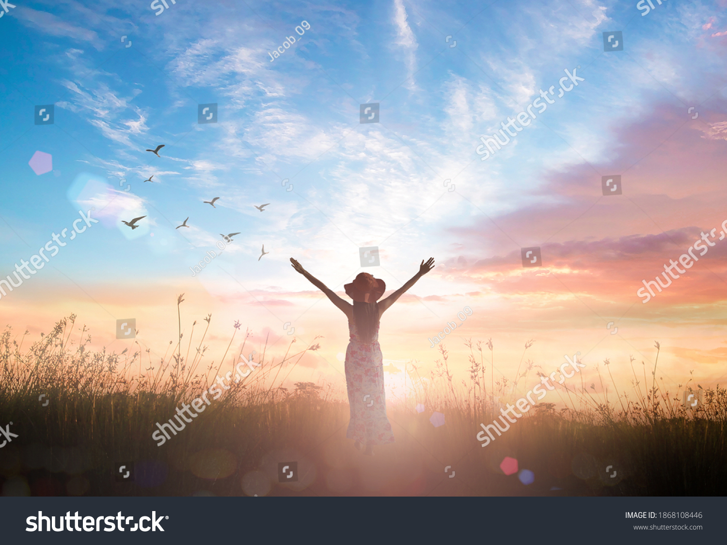 Surrender and praising concept: Silhouette of healthy Christian woman raised hands at meadow sunset background #1868108446