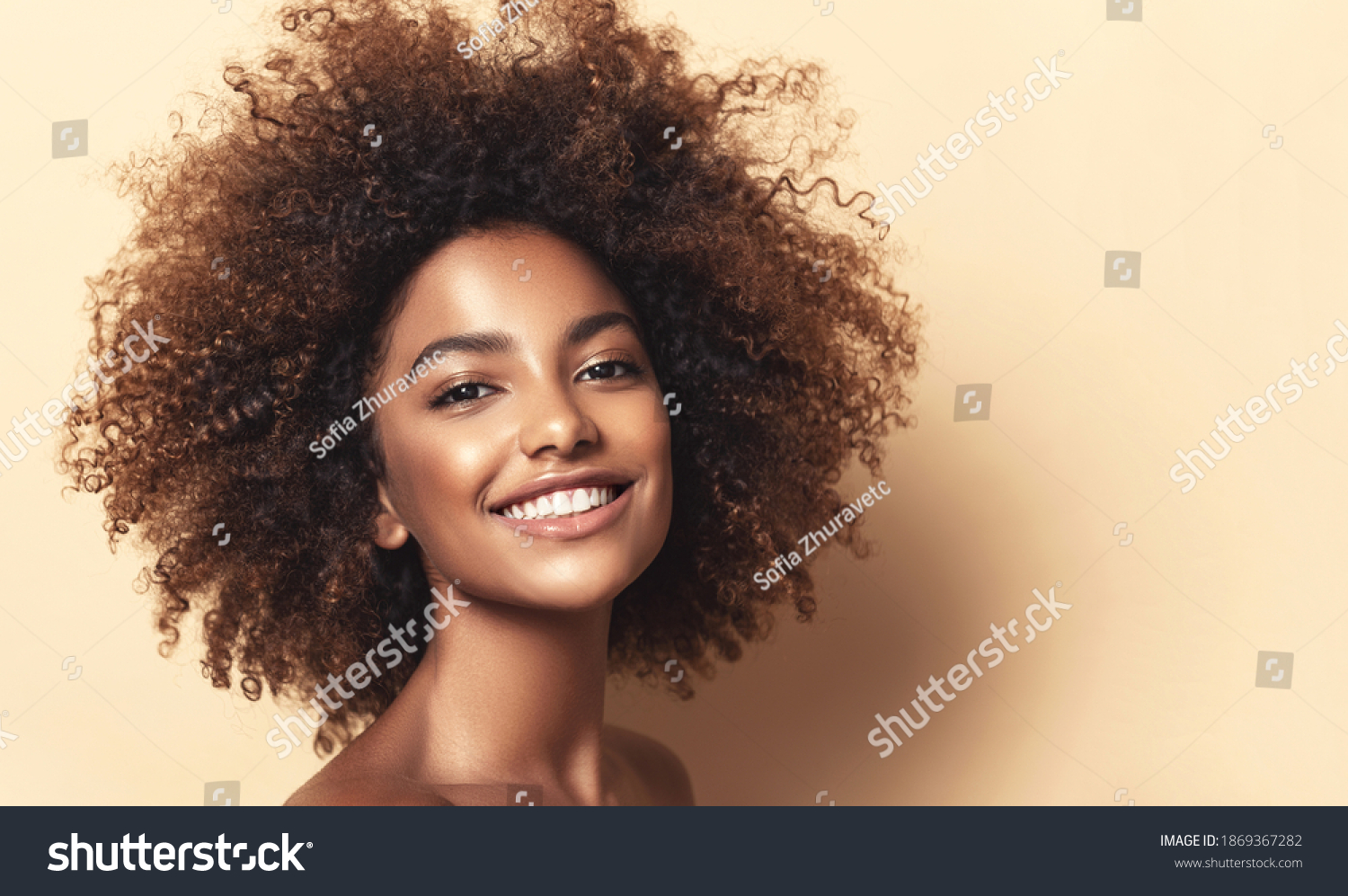 Beauty portrait of african american girl with clean healthy skin on beige background. Smiling dreamy beautiful black woman.Curly hair in afro style #1869367282