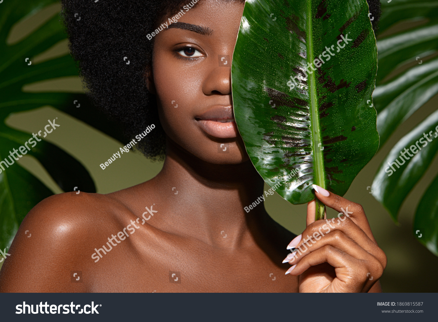 Beauty portrait of young beautiful african american woman with posing with banana leaf curly hair against green exotixc plants  background. Natural skin care concept #1869815587