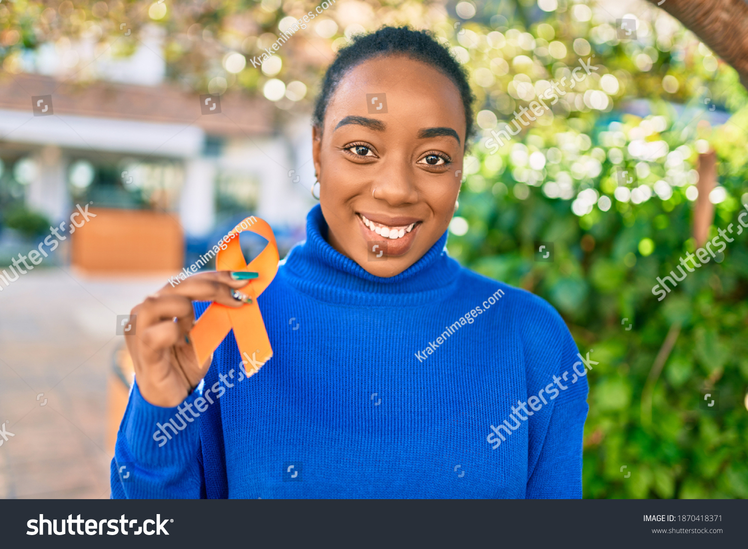 Young african american woman smiling happy holding orange awareness ribbon at the park. #1870418371