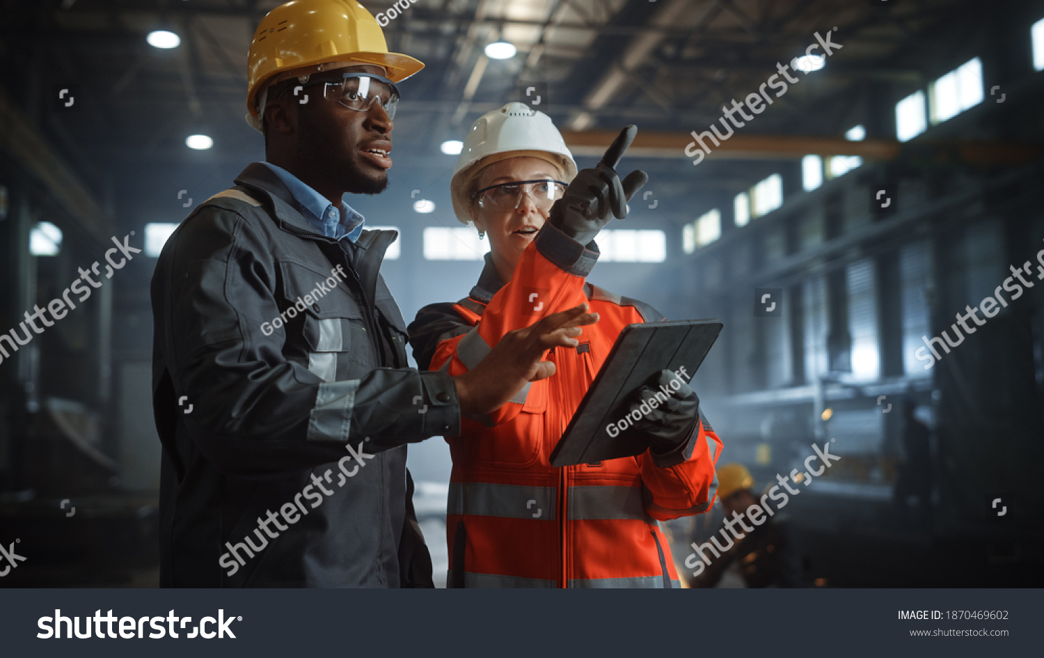 Two Heavy Industry Engineers Stand in Steel Metal Manufacturing Factory, Use Digital Tablet Computer and Have a Discussion. Black African American Industrial Specialist Talk to Female Technician. #1870469602