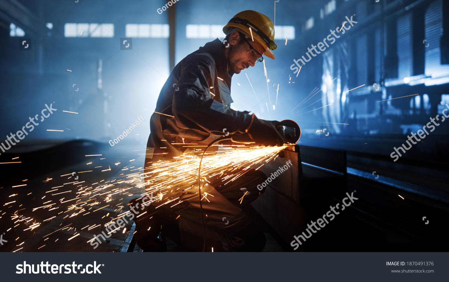 Heavy Industry Engineering Factory Interior with Industrial Worker Using Angle Grinder and Cutting a Metal Tube. Contractor in Safety Uniform and Hard Hat Manufacturing Metal Structures. #1870491376