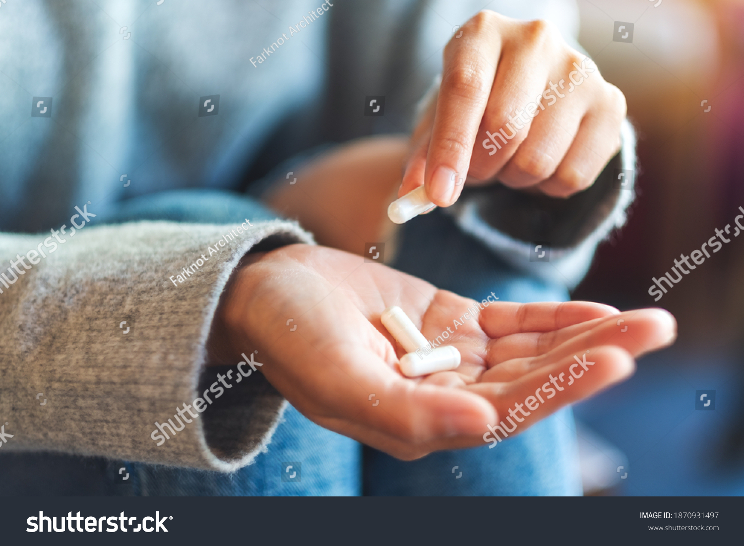 Closeup image of a woman holding and picking white medicine capsules in hand #1870931497