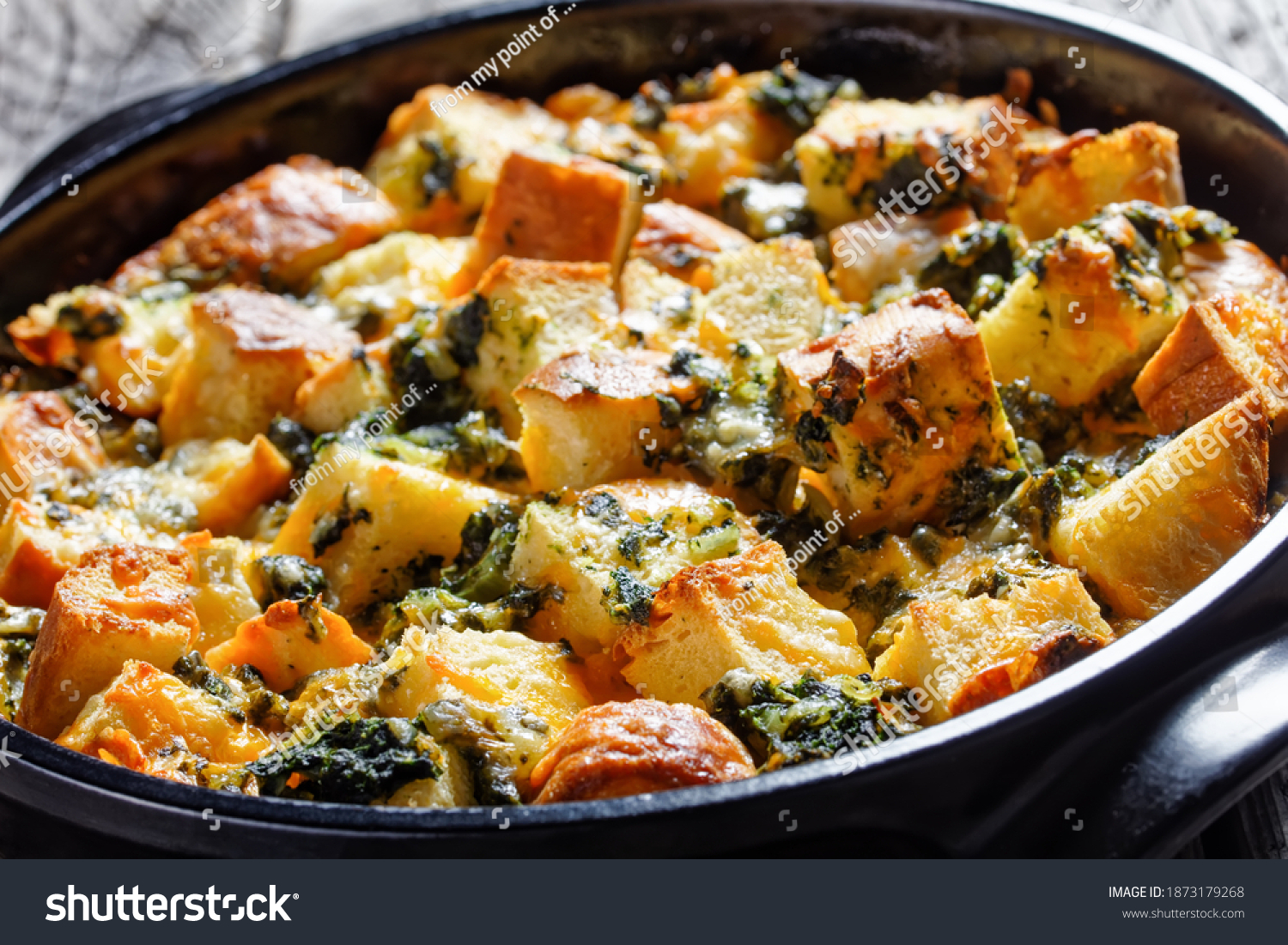 Italian spinach strata of soaked overnight cubed sandwich bread and baked with chopped spinach and shredded cheese with mustard served on a black baking dish on a wooden background, top view #1873179268