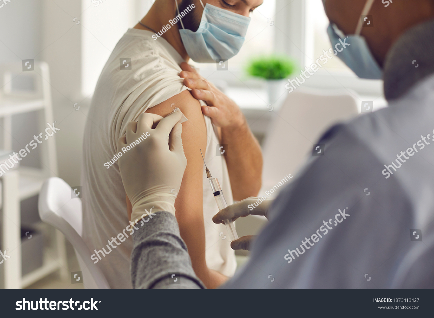 Immunization and disease prevention concept. Doctor giving antivirus injection to young man. Close-up patient in medical face mask getting flu or Covid-19 antiviral vaccine during vaccination campaign #1873413427