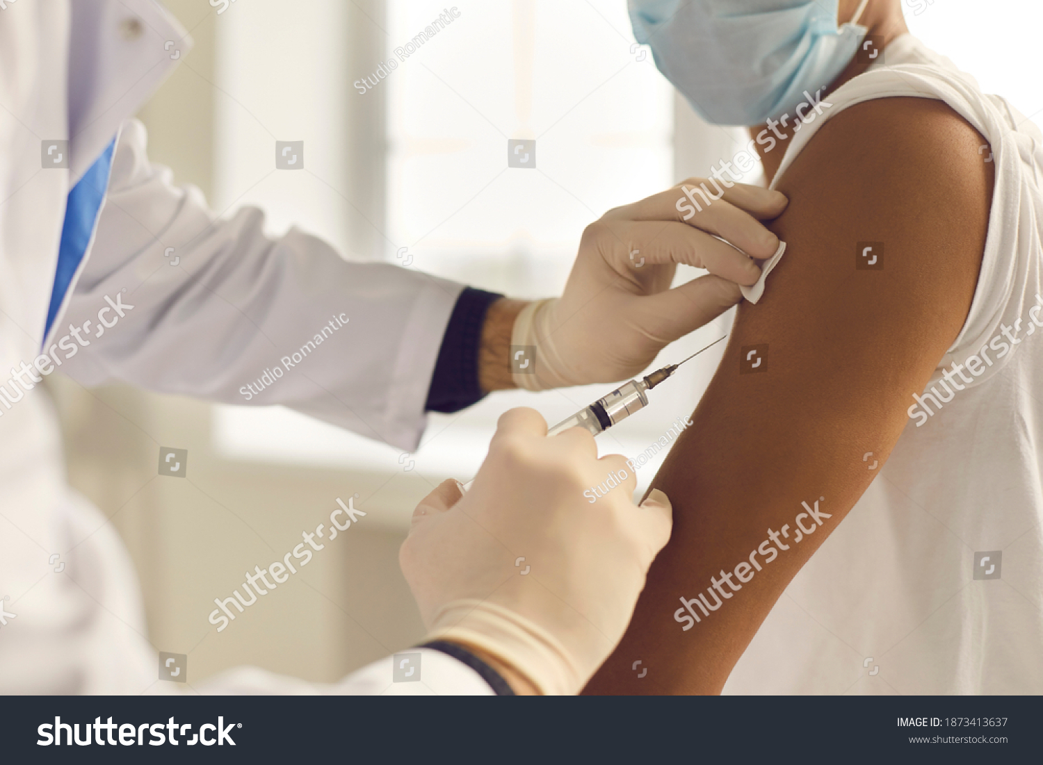 Doctor in medical gloves giving Covid-19, AIDS or flu antivirus vaccine shot to African-American patient. Close-up of hands holding syringe and cleaning skin on upper arm before antiviral injection #1873413637