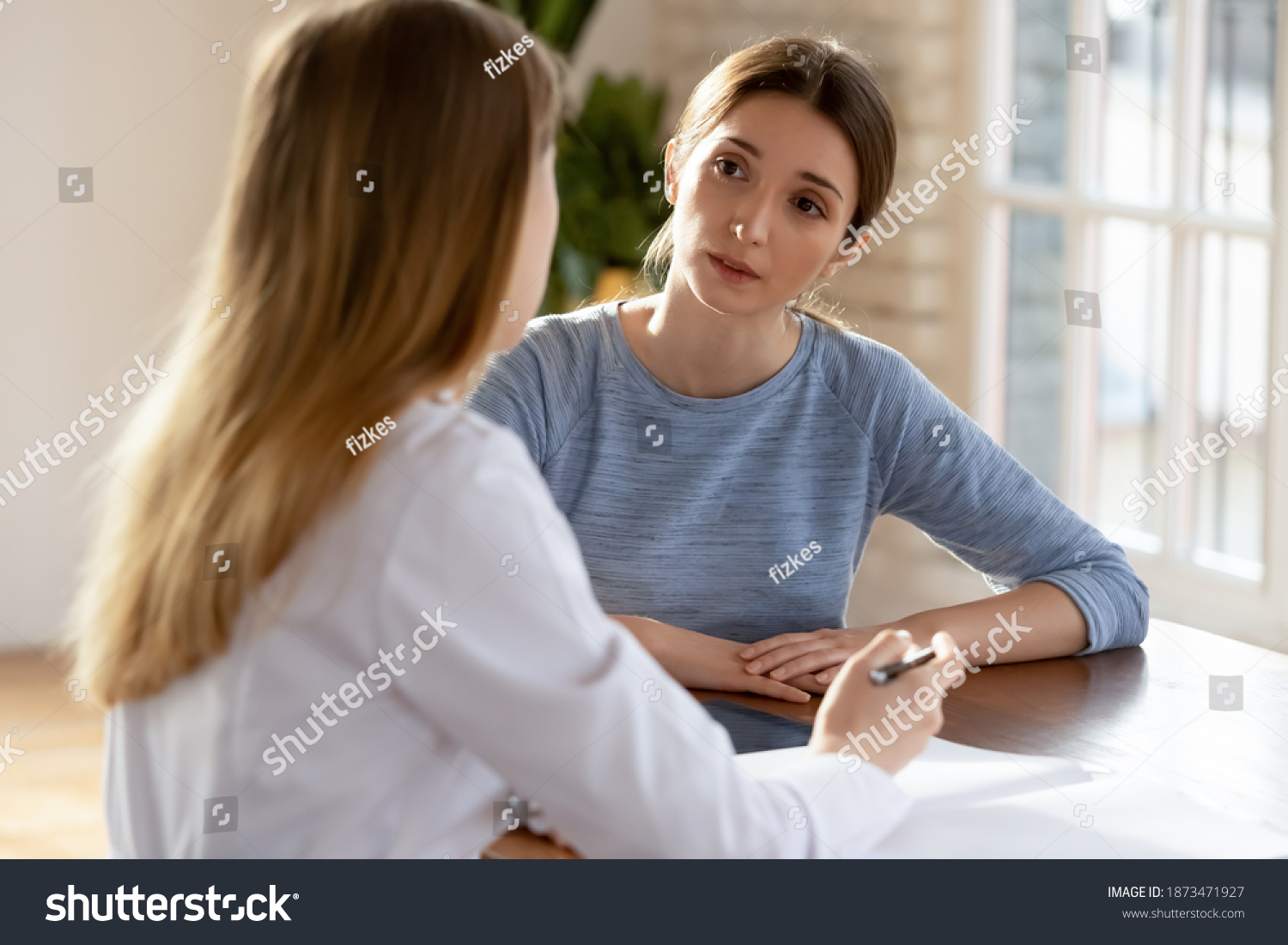 Young Caucasian female patient talk with nurse or GP at consultation in private hospital. Worried millennial woman consult speak with doctor in white medical uniform in clinic. Healthcare concept. #1873471927