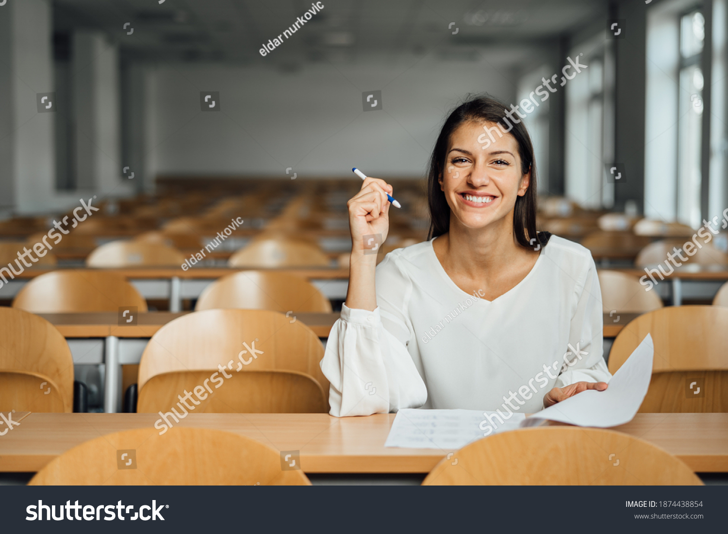 Knowledgable smiling student taking an easy exam in an empty amphitheater. An optimistic student taking an in-class test. Happy woman having stress free education evaluation.Essay exam inspiration. #1874438854