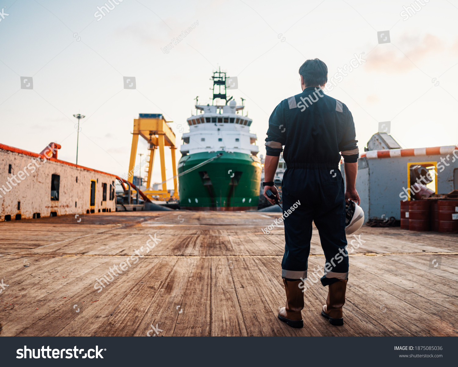 Marine Deck Officer or Chief mate on deck of offshore vessel or ship , wearing PPE personal protective equipment - helmet, coverall. Ship is on background #1875085036