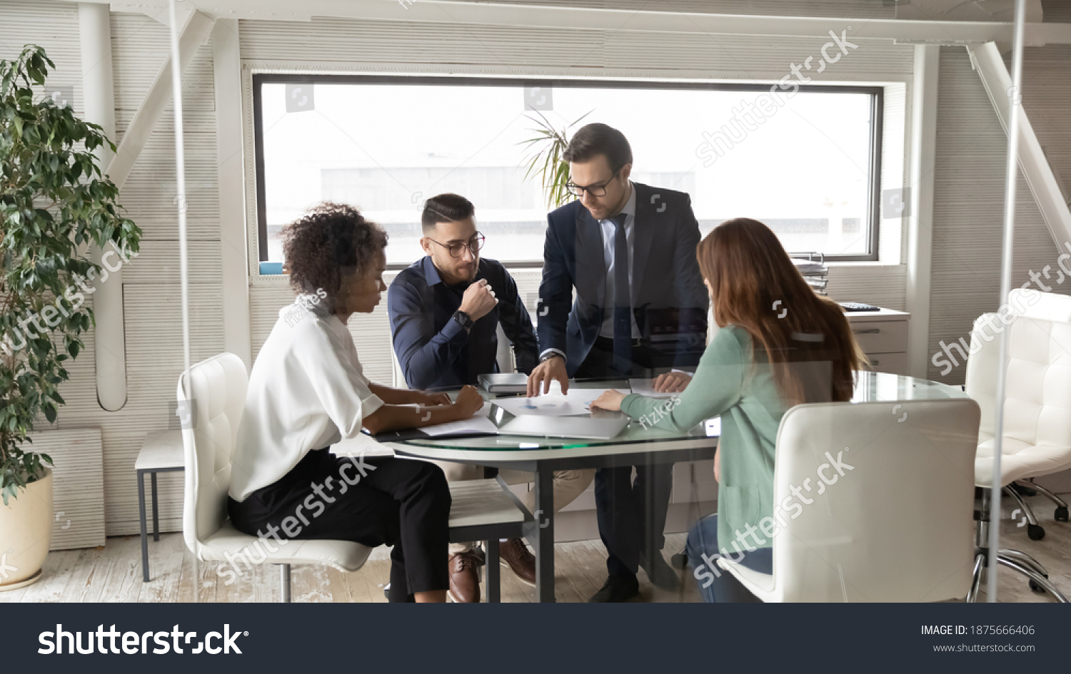 Multiracial businesspeople talk brainstorm discuss company financial statistics document at team meeting in office. Motivated multiethnic colleagues gather in boardroom consider paperwork at briefing. #1875666406