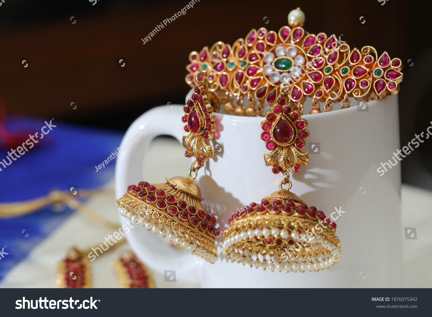 close up of head clip and a pair of temple jewelry arranged on a white porcelain cup #1876975342
