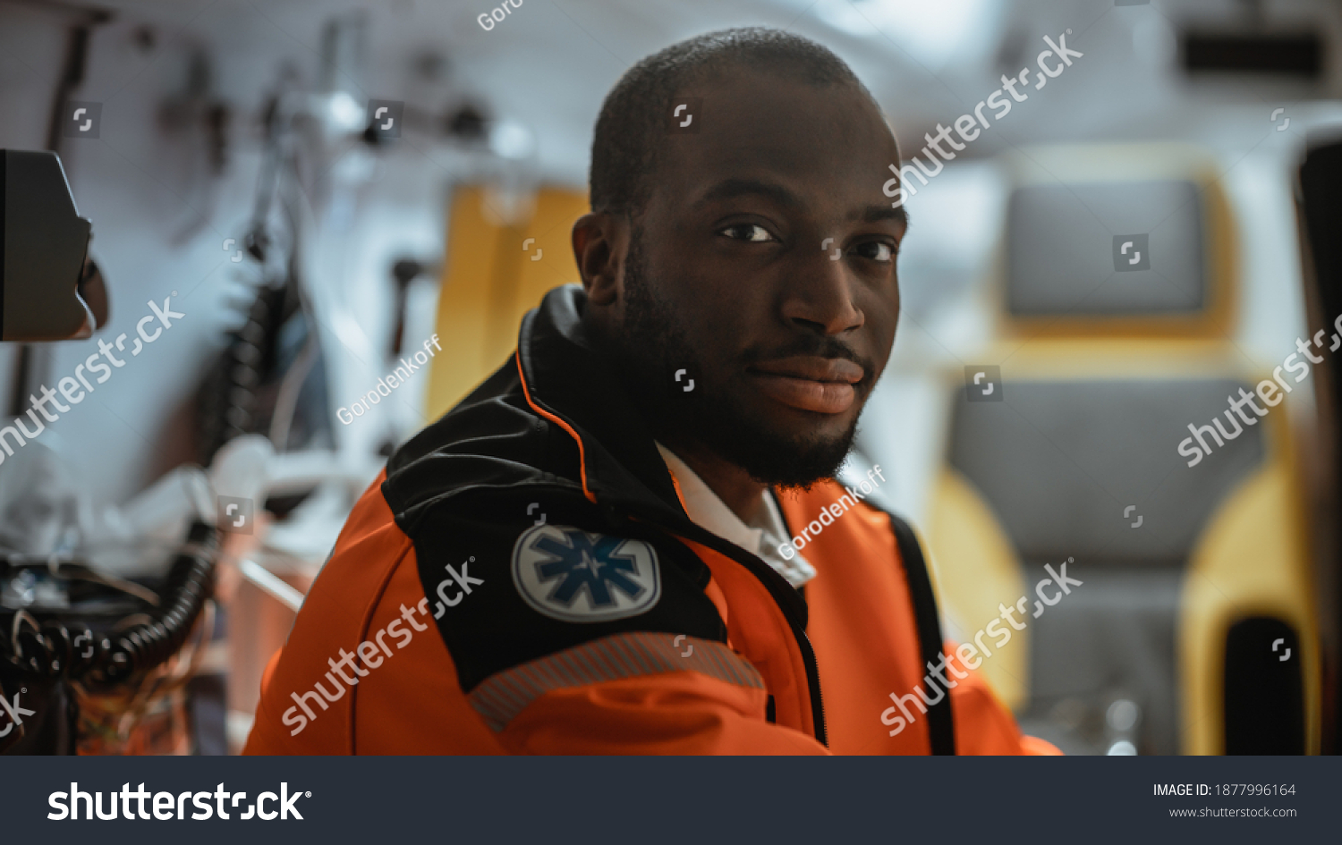 Black African American Paramedic Looking into Camera in an Ambulance Vehicle Going for Emergency. Emergency Medical Technicians are on Their Way to a Call Outside the Healthcare Hospital. #1877996164