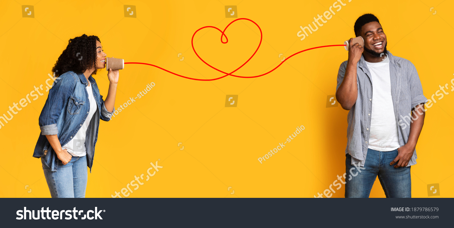 Love message. Loving african american woman telling romantic words to boyfriend through tin can phone with heart shaped string, standing together over yellow background, creative collage, panorama #1879786579