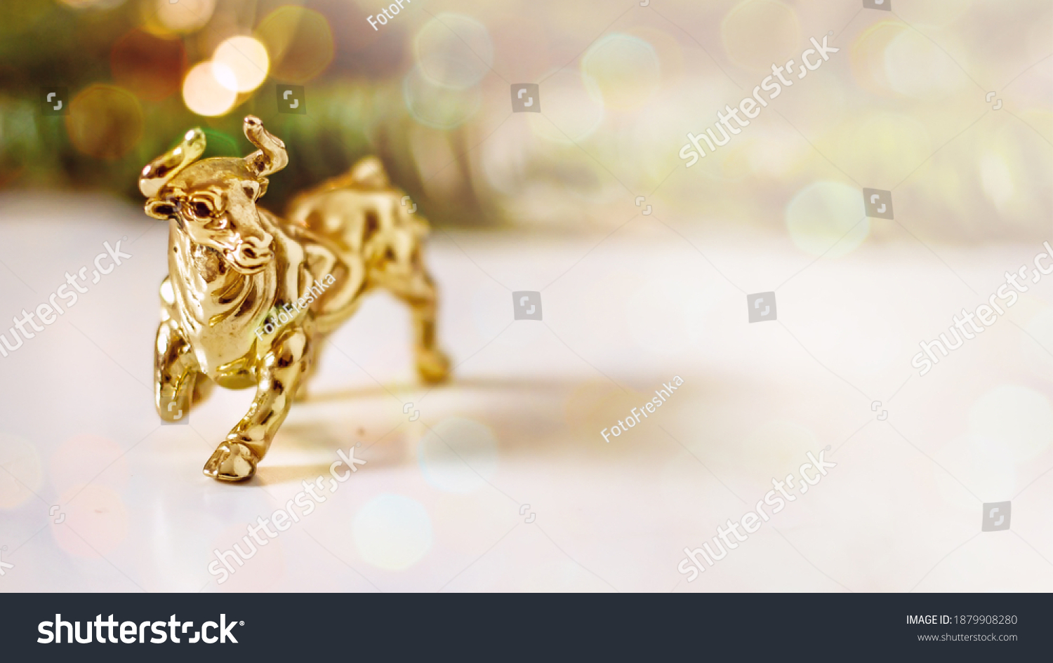 Golden calf, golden bull.Chinese new year of the bull. Year of the bull according to the Chinese calendar 2021. Souvenir bull made of gold metal on a background of fir branches with bokeh effect #1879908280