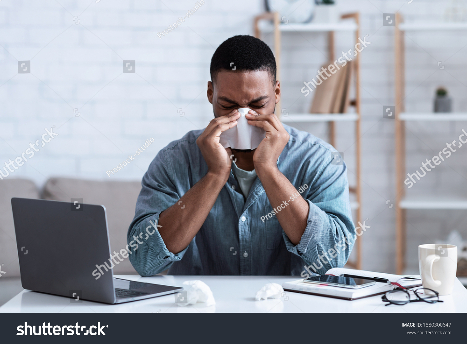 Sick Black Guy Working In Office, Sitting At Laptop And Blowing Nose In Paper Napkin Indoors. Ill Employee Concept. African Man Having Cold, Rhinitis And Sinusitis Symptoms At Work. #1880300647