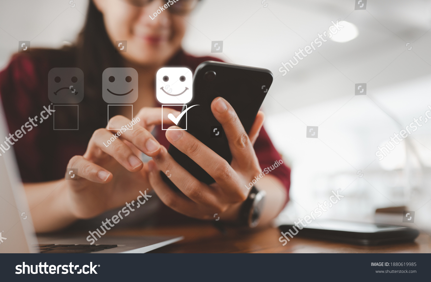 Customer service evaluation concept. smiling Asian female Is using a smartphone And she is pressing face emoticon smiling in satisfaction on virtual touch screen. #1880619985
