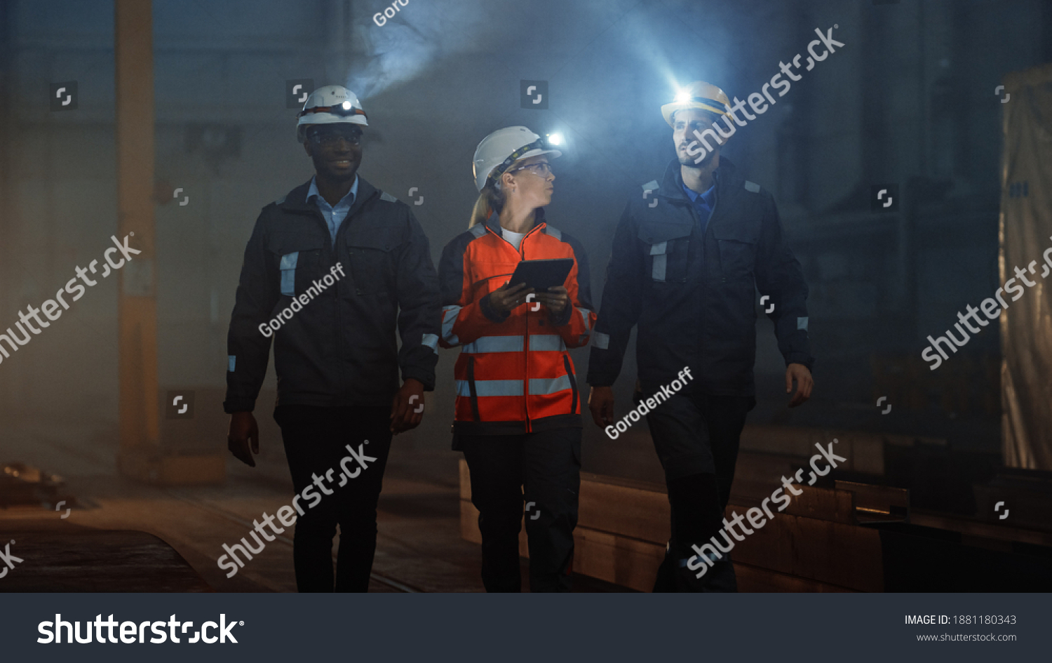 Three Diverse Multicultural Heavy Industry Engineers and Workers in Uniform Walk in Dark Steel Factory Using Flashlights on Their Hard Hats. Female Industrial Contractor is Using a Tablet Computer. #1881180343