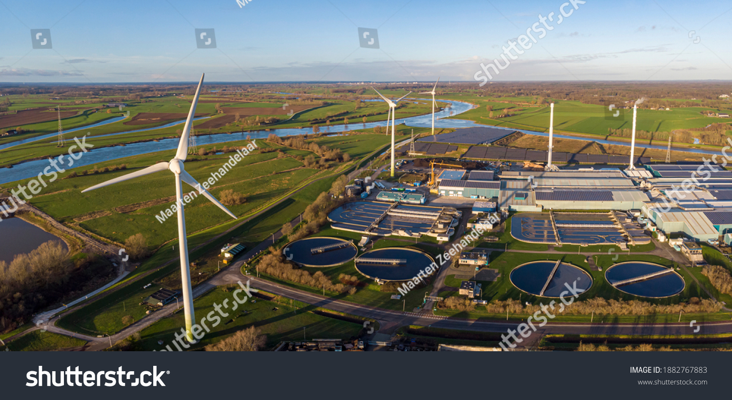 Wind turbines, water treatment and bio energy facility and solar panels in The Netherlands part of sustainable industry in Dutch flat river landscape against blue sky. Aerial circular economy concept. #1882767883