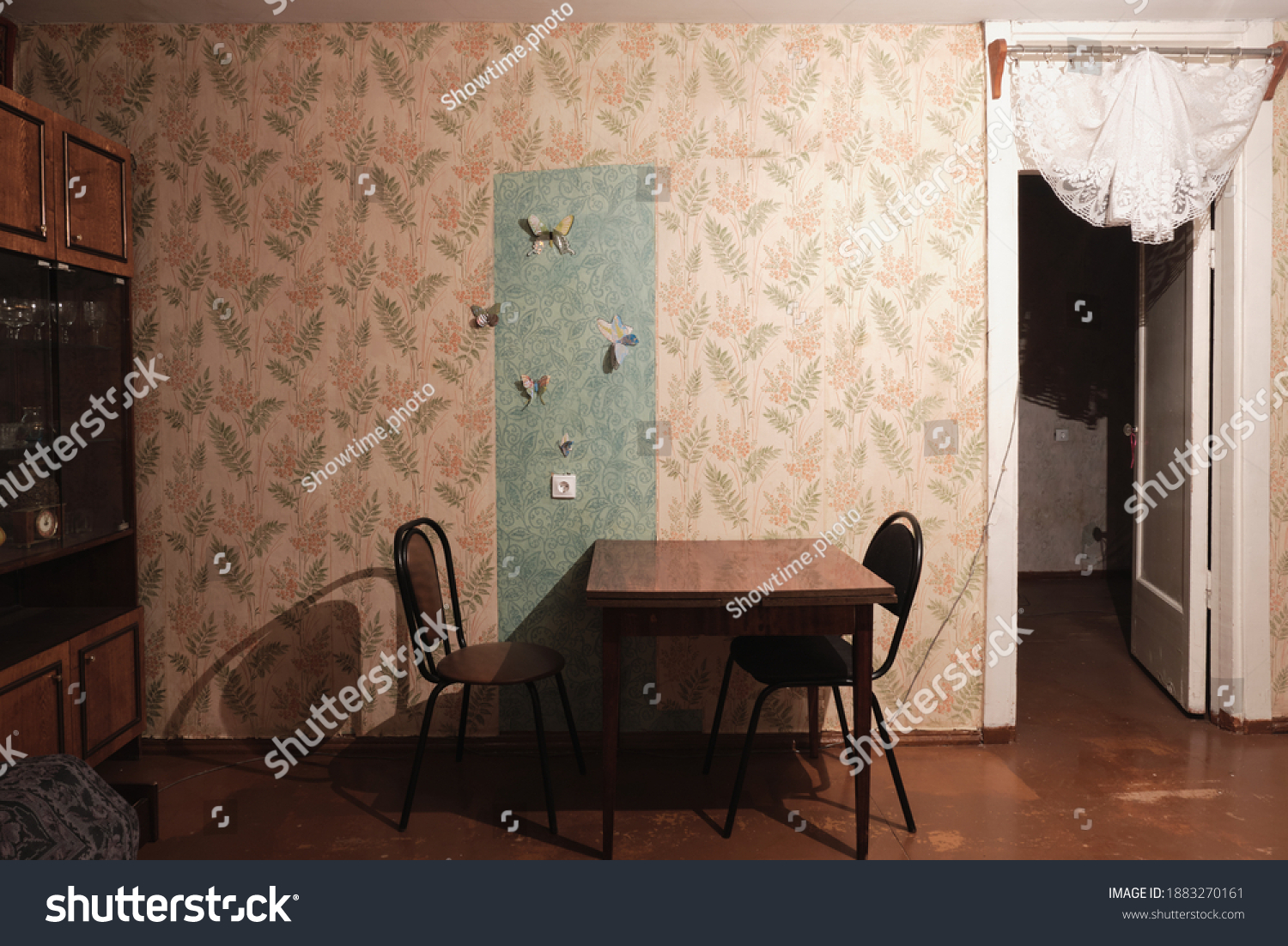 Example of Old Soviet Russian poor interior in Khruschev House. Aged  sideboard, table, chairs, sofa. Shabby floor. Tattered wallpaper on the wall. Paper butterflies as decor. Apartment of pensioners. #1883270161