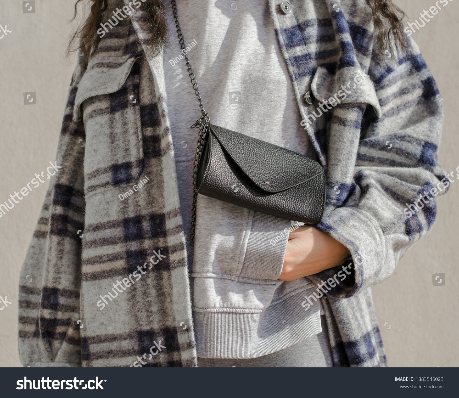 Woman wearing plaid trendy jacket on a gray hoodie with a black leather bag with her hand in her pocket. #1883546023