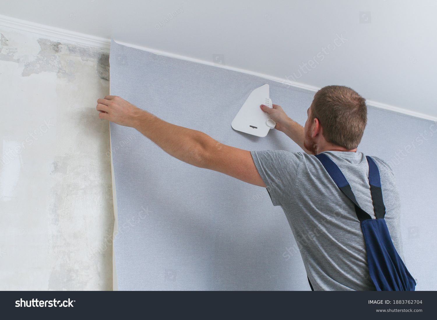 Wallpapering. A man glues gray vinyl wallpaper on a non-woven backing. Renovation of the room. Hang wallpaper. Home repairs. #1883762704