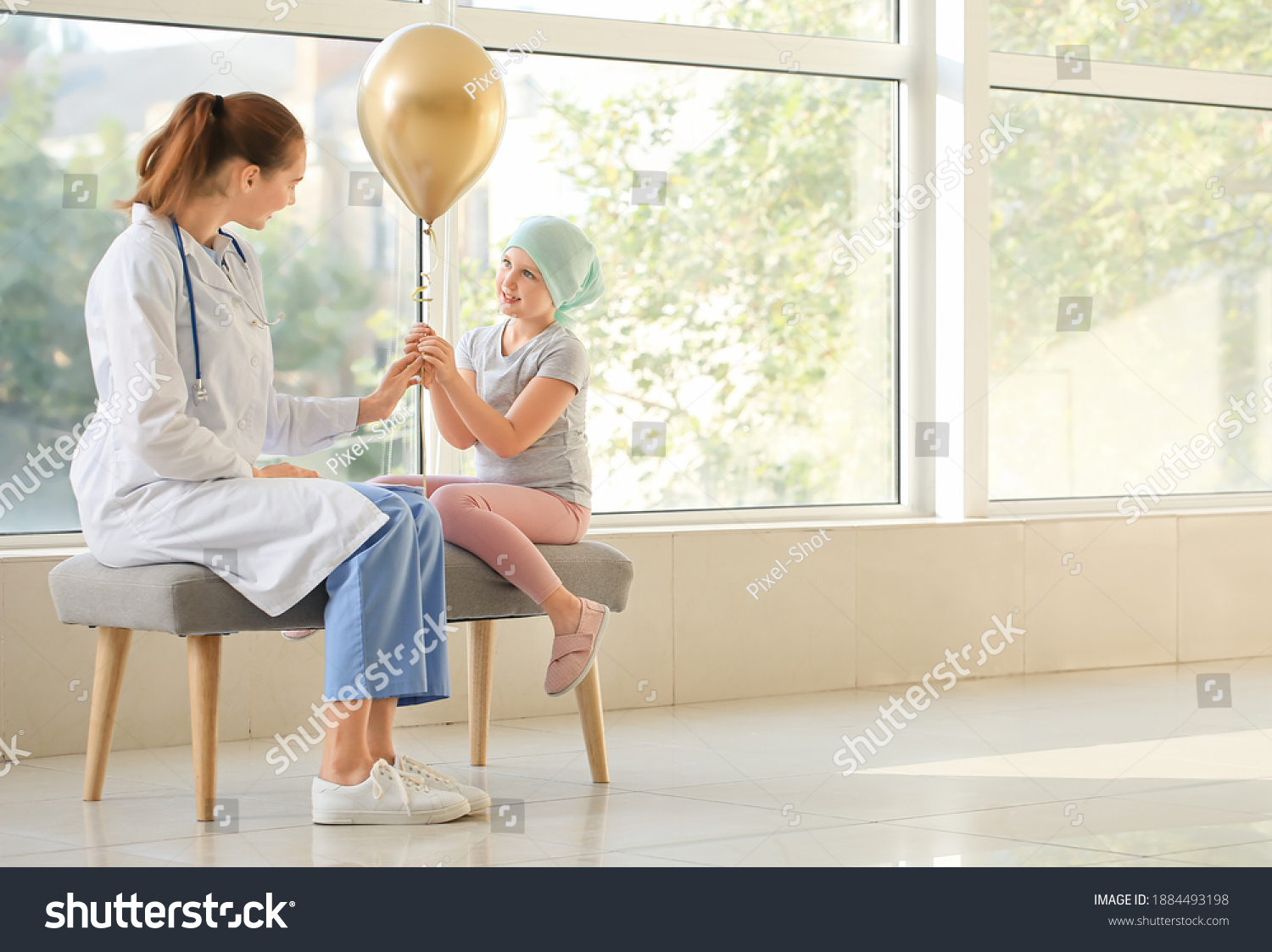 Doctor and little girl with golden balloon in clinic. Childhood cancer awareness concept #1884493198