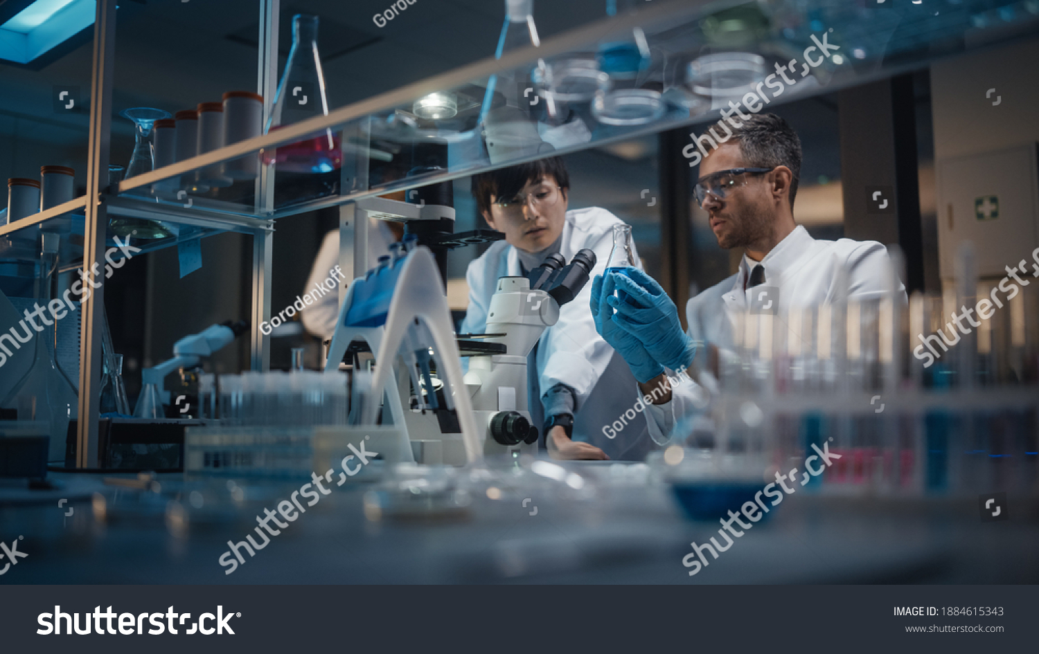 Modern Medical Research Laboratory: Team of East Asian and Caucasian Scientists Work on Laptop, do Data Analysis, Use Microscope. Advanced Lab for Medicine, Biotechnology Development. Evening Time #1884615343